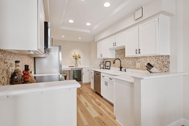 kitchen featuring a raised ceiling, a sink, light wood-type flooring, beverage cooler, and dishwasher