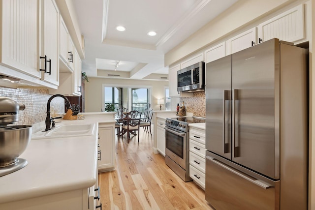 kitchen featuring light wood finished floors, appliances with stainless steel finishes, a tray ceiling, light countertops, and a sink