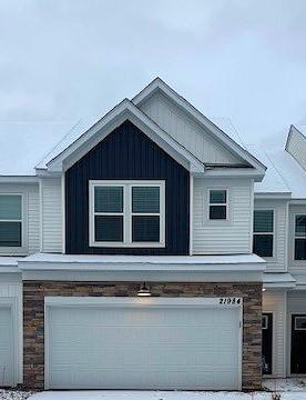 view of side of home featuring board and batten siding, stone siding, driveway, and a garage