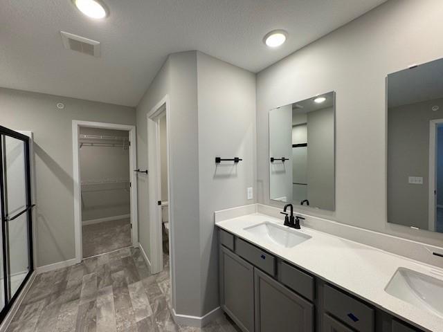 bathroom featuring visible vents, a sink, a spacious closet, and double vanity