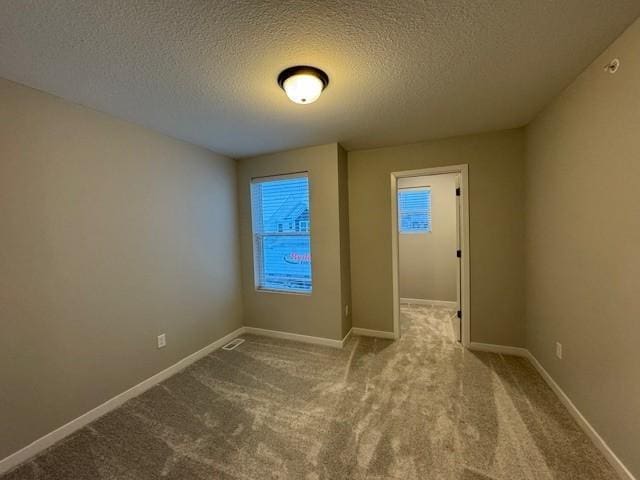 empty room with carpet floors, a textured ceiling, and baseboards