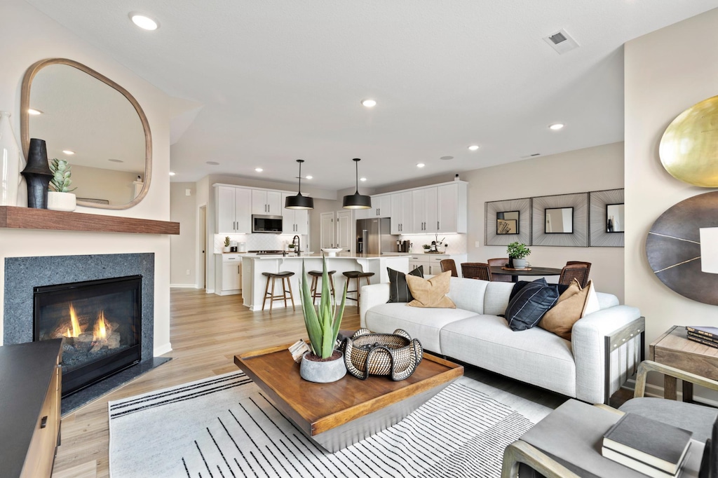 living room featuring light wood-type flooring, a glass covered fireplace, visible vents, and recessed lighting