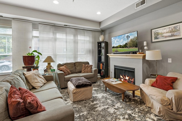 living area featuring recessed lighting, a warm lit fireplace, and visible vents