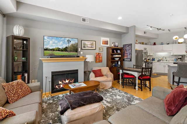 living area featuring light wood-type flooring, a warm lit fireplace, visible vents, and recessed lighting