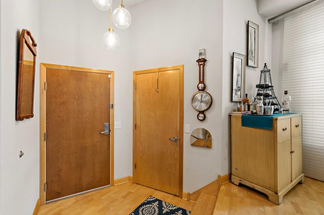 foyer featuring baseboards, light wood-style flooring, and a high ceiling