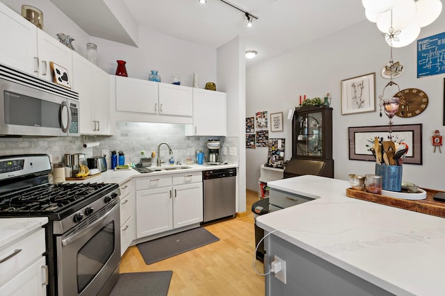 kitchen featuring light wood-style flooring, stainless steel appliances, a sink, white cabinets, and backsplash