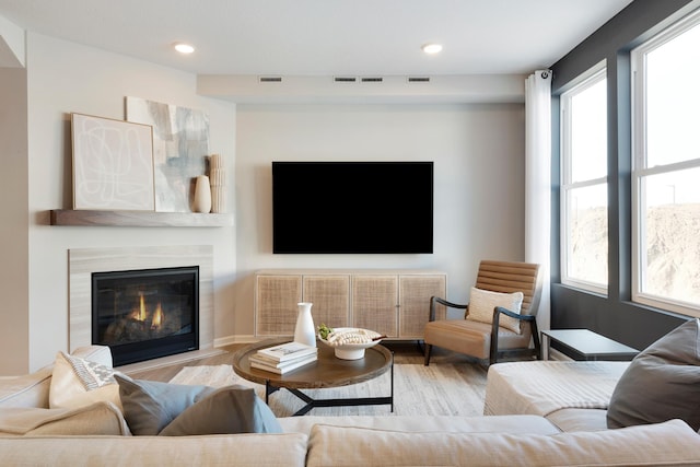 living area with a wealth of natural light, visible vents, wood finished floors, and a glass covered fireplace