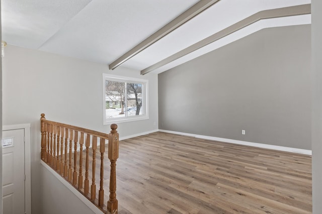 unfurnished room with lofted ceiling with beams, wood finished floors, and baseboards