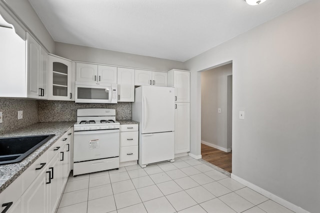 kitchen featuring tasteful backsplash, white appliances, glass insert cabinets, and a sink