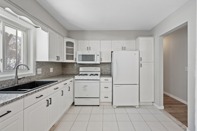 kitchen featuring glass insert cabinets, light tile patterned floors, decorative backsplash, white appliances, and a sink