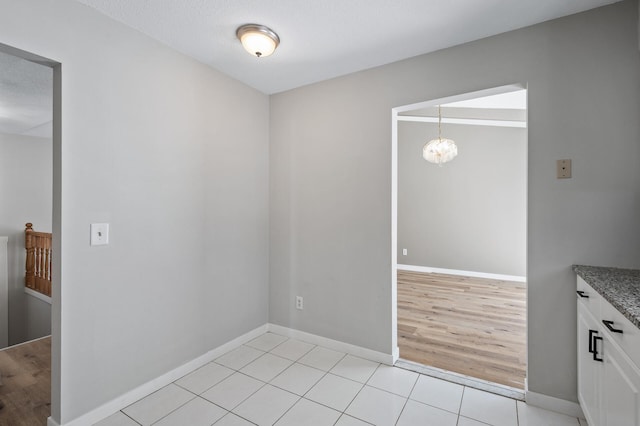 unfurnished room with baseboards, a notable chandelier, and light tile patterned flooring