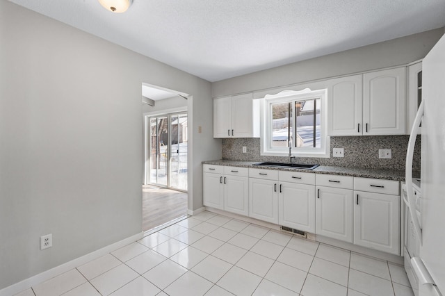 kitchen featuring a sink, backsplash, a healthy amount of sunlight, and white cabinets