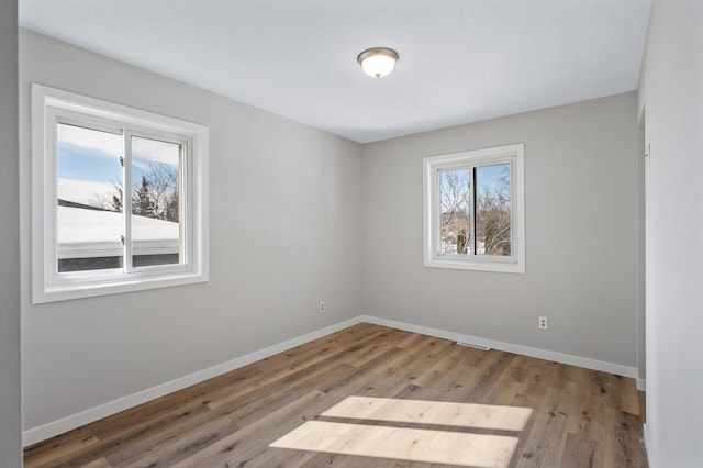 empty room with plenty of natural light, baseboards, and wood finished floors