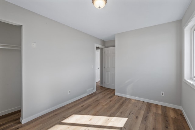 unfurnished bedroom featuring visible vents, baseboards, a closet, and wood finished floors