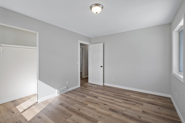 unfurnished bedroom with a closet, visible vents, baseboards, and wood finished floors