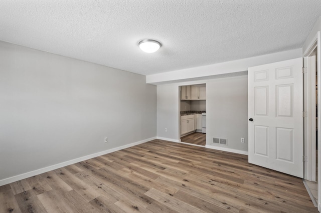 unfurnished bedroom featuring visible vents, a textured ceiling, wood finished floors, connected bathroom, and baseboards