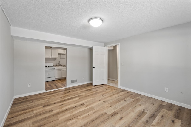 unfurnished bedroom with light wood-type flooring, visible vents, a sink, a textured ceiling, and baseboards