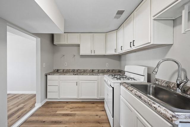 kitchen with visible vents, gas range gas stove, light wood-style floors, white cabinets, and a sink