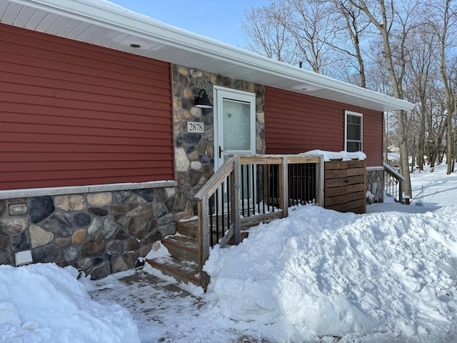 snow covered property entrance featuring stone siding