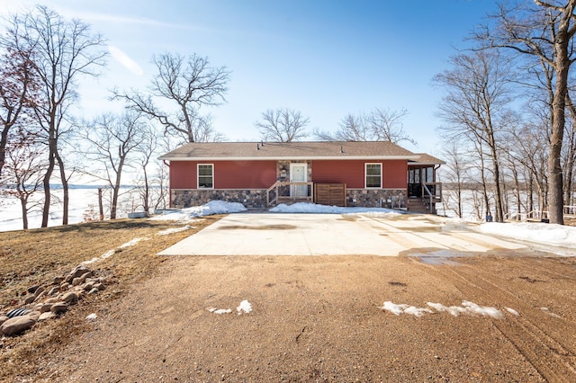 snow covered house with driveway and stone siding