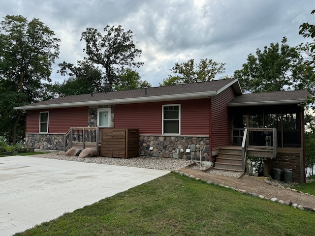 back of property with stone siding, a lawn, and a sunroom