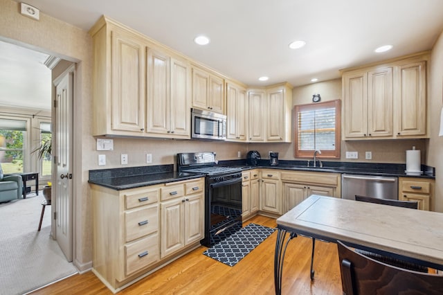 kitchen featuring dark countertops, appliances with stainless steel finishes, light brown cabinetry, light wood-type flooring, and a sink