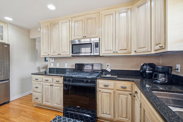 kitchen with light wood finished floors, recessed lighting, appliances with stainless steel finishes, light brown cabinets, and dark stone counters