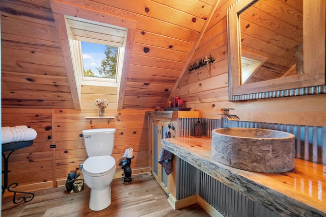 bathroom with vaulted ceiling with skylight, wood finished floors, toilet, and wooden walls