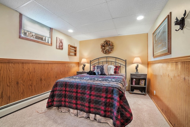 carpeted bedroom with a wainscoted wall, a paneled ceiling, recessed lighting, a baseboard heating unit, and wood walls