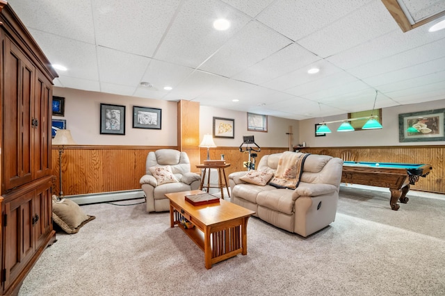 carpeted living area featuring a wainscoted wall, wooden walls, baseboard heating, and a drop ceiling