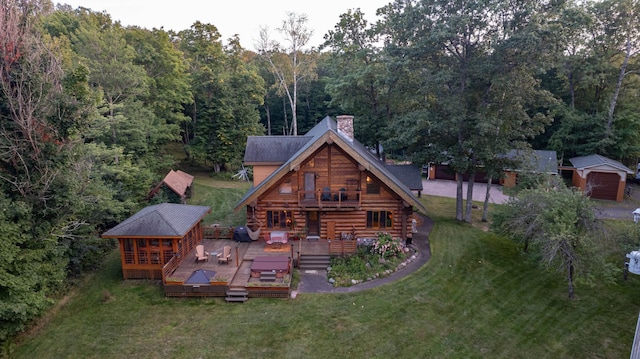 back of property with a yard, a chimney, a deck, a view of trees, and log siding