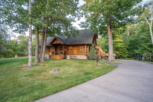 log cabin featuring a chimney, log siding, aphalt driveway, a front lawn, and a porch