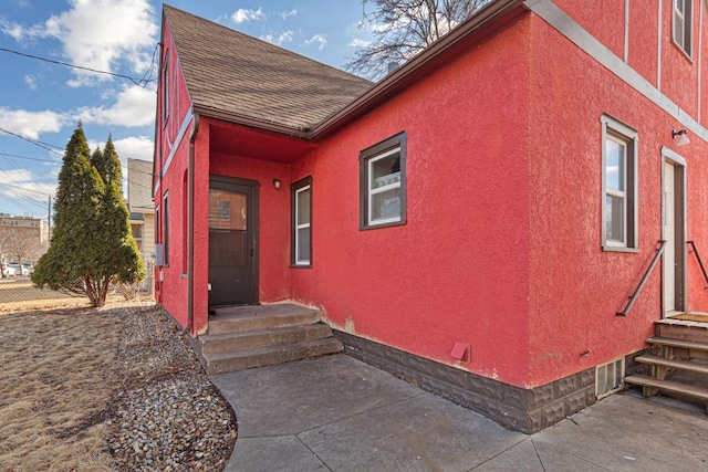 view of side of property featuring stucco siding, roof with shingles, and fence