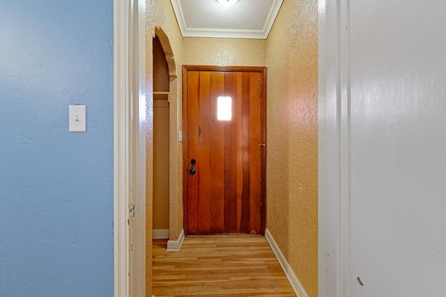 corridor with baseboards, ornamental molding, light wood-style floors, a textured wall, and arched walkways