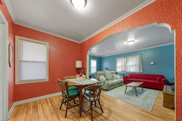 dining room with arched walkways, wood finished floors, a textured wall, and ornamental molding