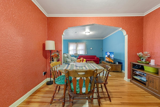 dining space featuring arched walkways, light wood-style flooring, and crown molding