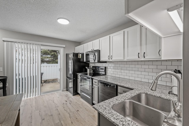 kitchen featuring white cabinets, a sink, light stone countertops, black appliances, and backsplash