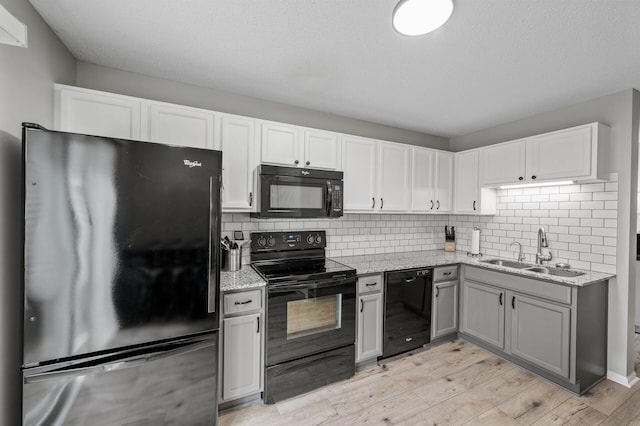 kitchen featuring black appliances, decorative backsplash, a sink, and light wood-style floors