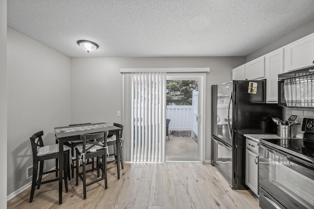 kitchen featuring a textured ceiling, light wood-style flooring, white cabinetry, baseboards, and black appliances