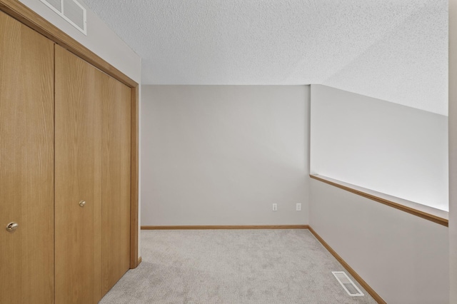 interior space featuring carpet floors, visible vents, vaulted ceiling, and a textured ceiling