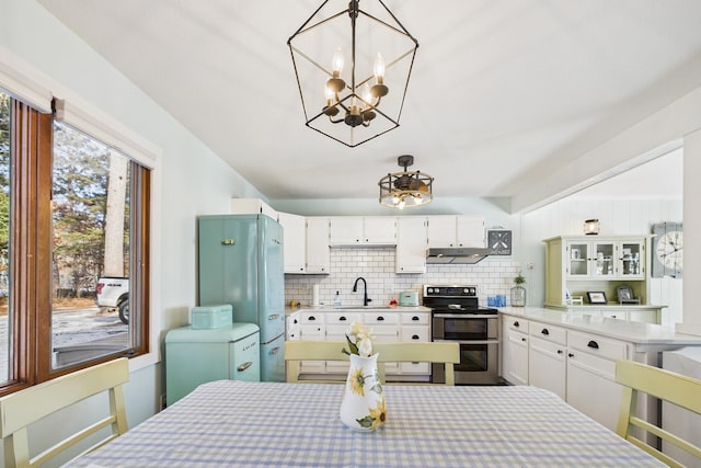 kitchen featuring an inviting chandelier, tasteful backsplash, ventilation hood, a sink, and range with two ovens