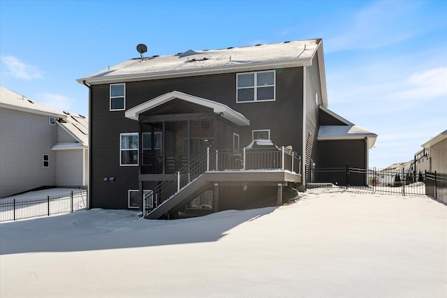 snow covered rear of property featuring a sunroom, fence, and stairway