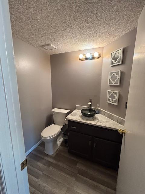 bathroom with toilet, a textured ceiling, vanity, wood finished floors, and baseboards