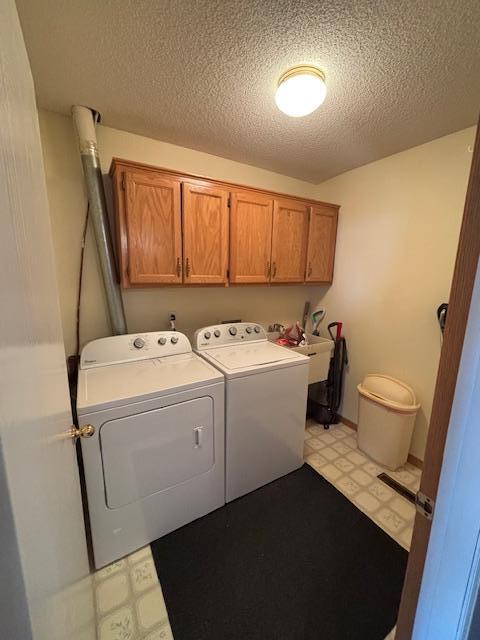 washroom with light floors, a textured ceiling, cabinet space, and independent washer and dryer