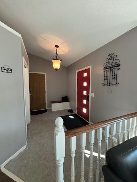 tiled foyer entrance featuring vaulted ceiling, baseboards, and stairs