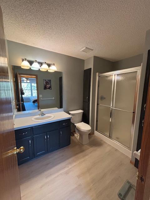 full bathroom featuring a stall shower, toilet, wood finished floors, a textured ceiling, and vanity