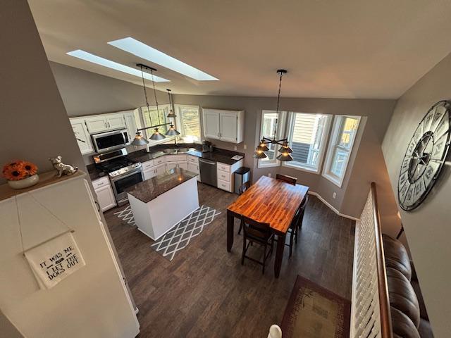 dining room with dark wood-style floors, lofted ceiling with skylight, baseboards, and an inviting chandelier