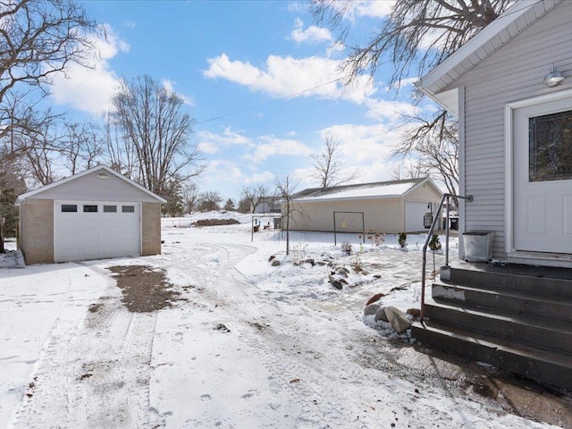 snowy yard with entry steps, a detached garage, and an outdoor structure