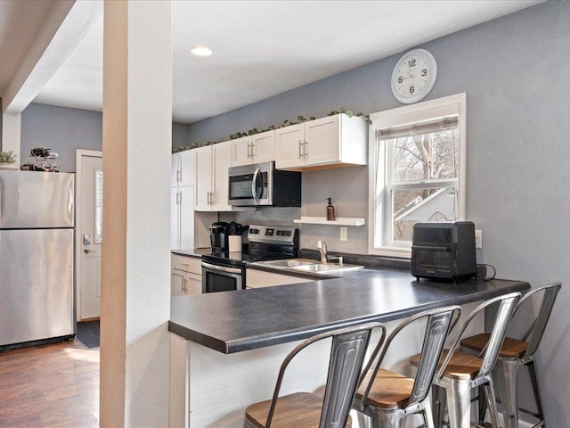 kitchen with a breakfast bar, a sink, white cabinetry, appliances with stainless steel finishes, and dark countertops