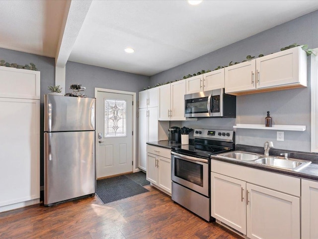 kitchen with appliances with stainless steel finishes, dark countertops, a sink, and dark wood finished floors